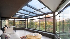 Un salón moderno con un amplio ventanal, un sofá, una mesa de centro y un trípode al fondo.