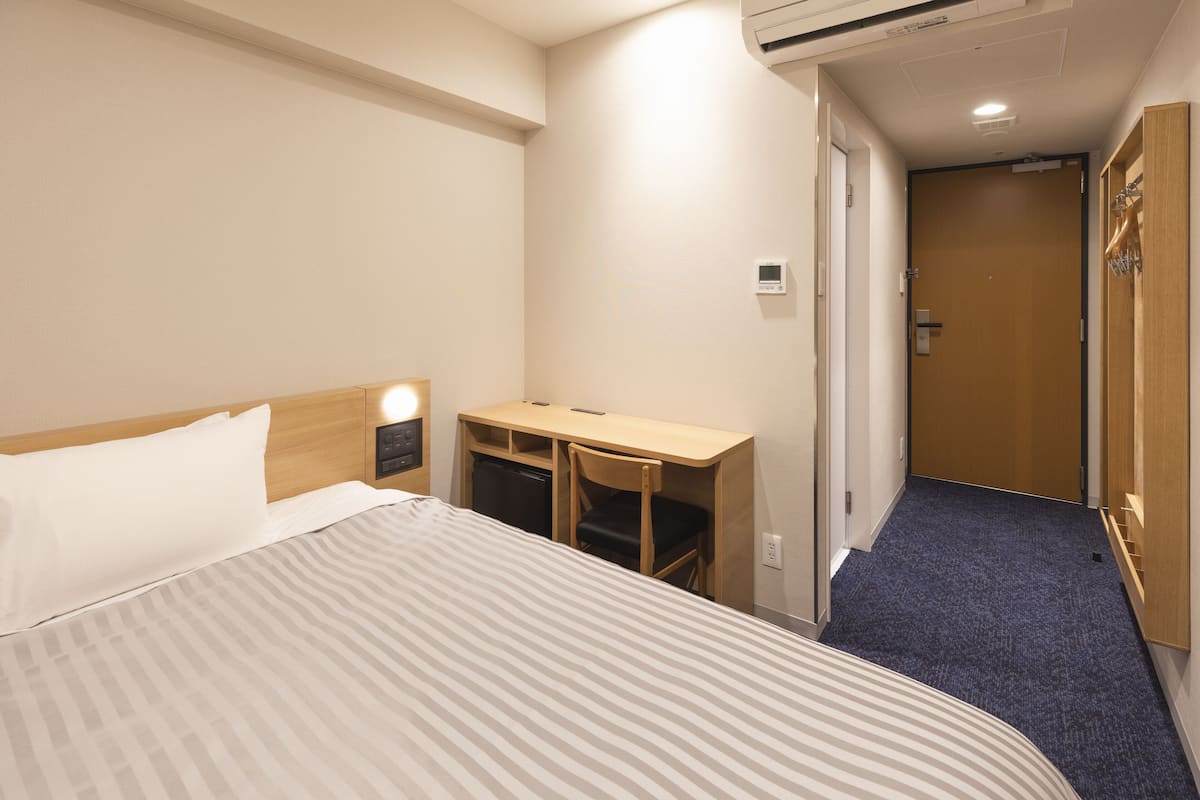 A hotel room with a bed, a desk, a chair, and a small kitchenette.