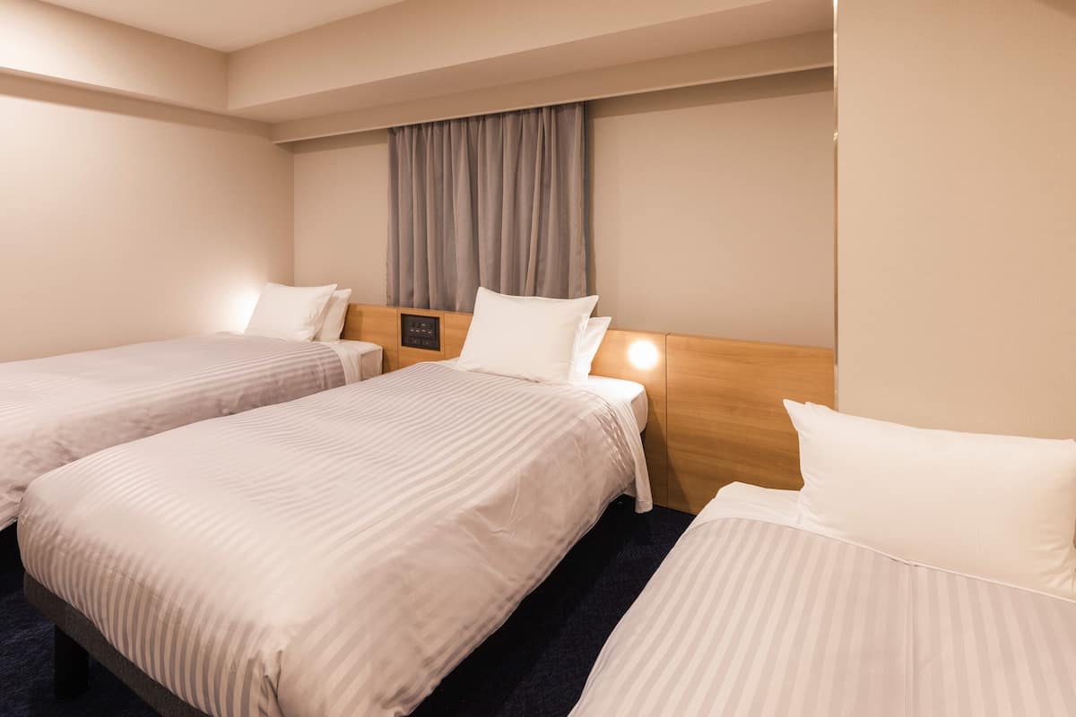 A hotel room with two single beds, a wooden headboard, a control panel, and a curtain.