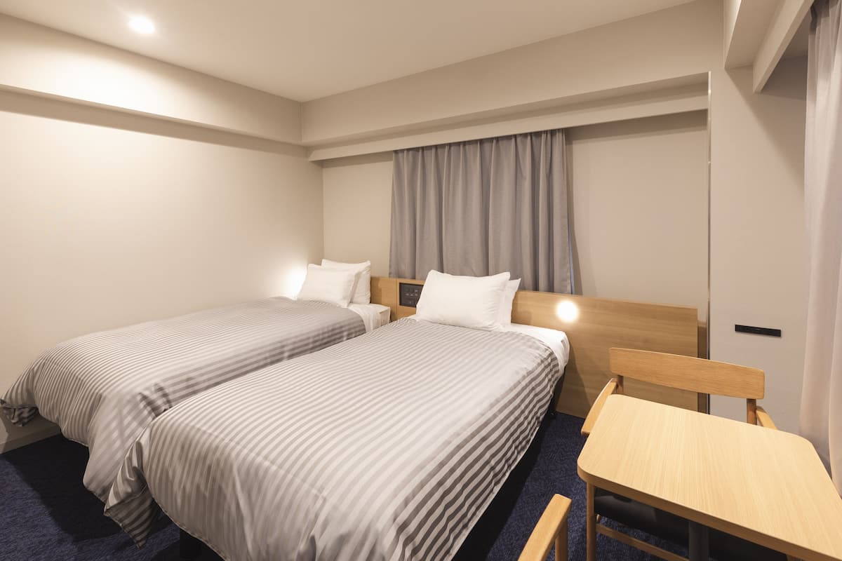 A hotel room with two single beds, a wooden headboard, a small desk, and a nightstand.