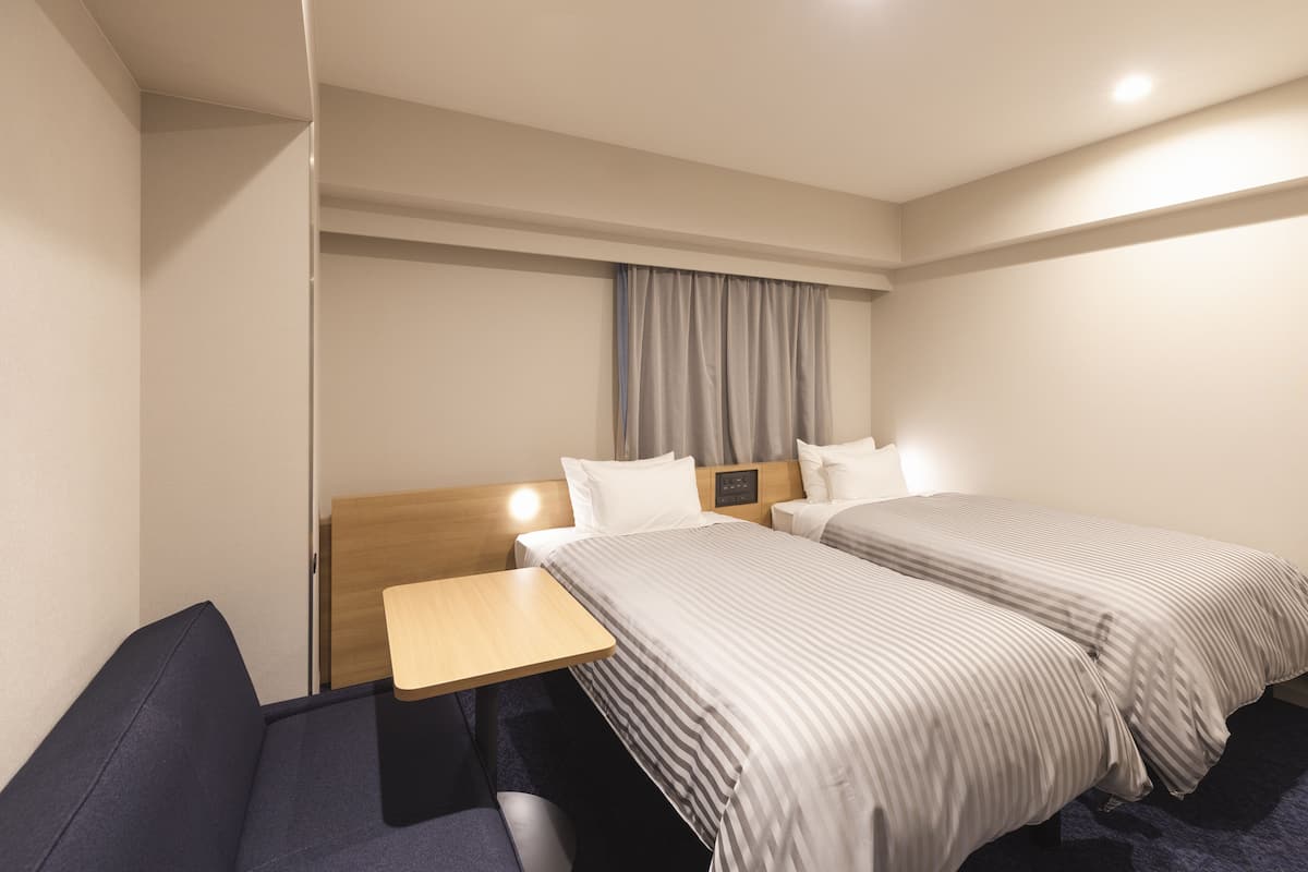 A hotel room with two beds, a desk, and a chair.