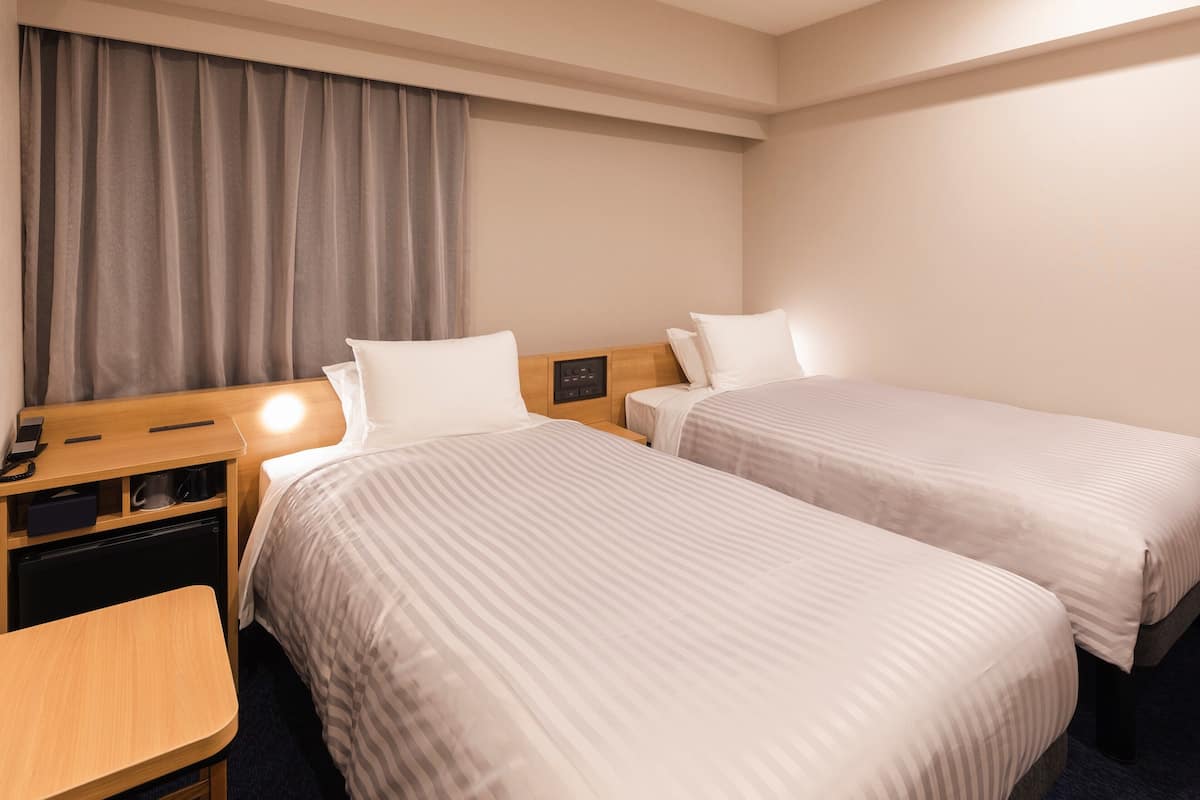 A hotel room with two beds, a wooden desk, a small table, and a curtain.