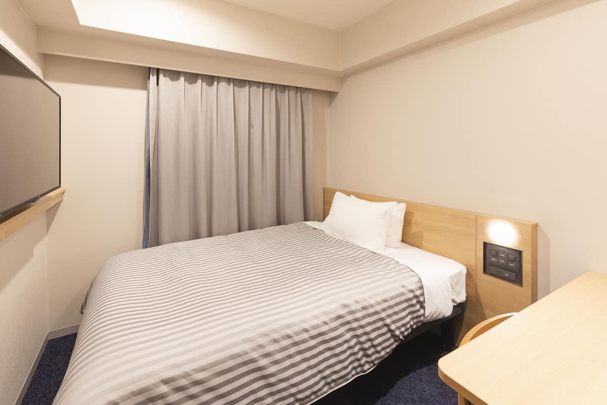 A hotel room with a bed, a desk, a TV, and a window with curtains.