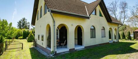 A two-story house with a tiled roof, arched doorways, and a small patio area.