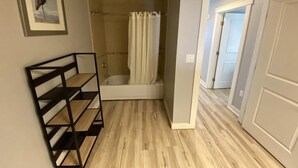 A bathroom with a shower, a wooden floor, a framed picture on the wall, and a door leading to another room. - Beautiful Beachfront luxury living at its best (Panama City Beach)