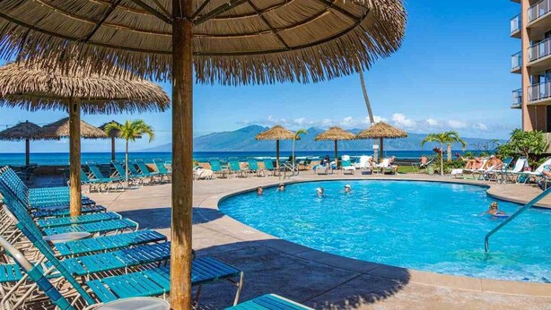 A pool area with lounge chairs and thatched umbrellas, overlooking a body of water. - Oceanview Soothing Waves Kaanapali West MAUI STUDIO (Lahaina)