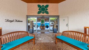 A lobby with two wooden benches with blue cushions, a large green emblem on the wall, and a sign reading "Royal Kahana". - Oceanview Soothing Waves Kaanapali West MAUI STUDIO (Lahaina)