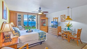 A bedroom with a bed, a desk, a chair, a table, and a view of the ocean. - Oceanview Soothing Waves Kaanapali West MAUI STUDIO (Lahaina)