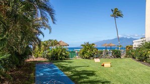 A garden with a shuffleboard court, palm trees, and a view of the ocean. - Oceanview Soothing Waves Kaanapali West MAUI STUDIO (Lahaina)