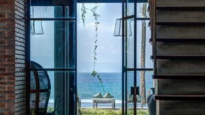 Een open glazen deur die leidt naar een terras met uitzicht op zee, een bank en een stoel.