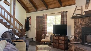 A cozy living room with a wooden ceiling, a fireplace, a television, and a staircase. - Treasure in the Trees (Twain Harte)