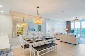 Un salon moderne avec un coin repas, des meubles blancs et une grande fenêtre donnant sur un paysage.