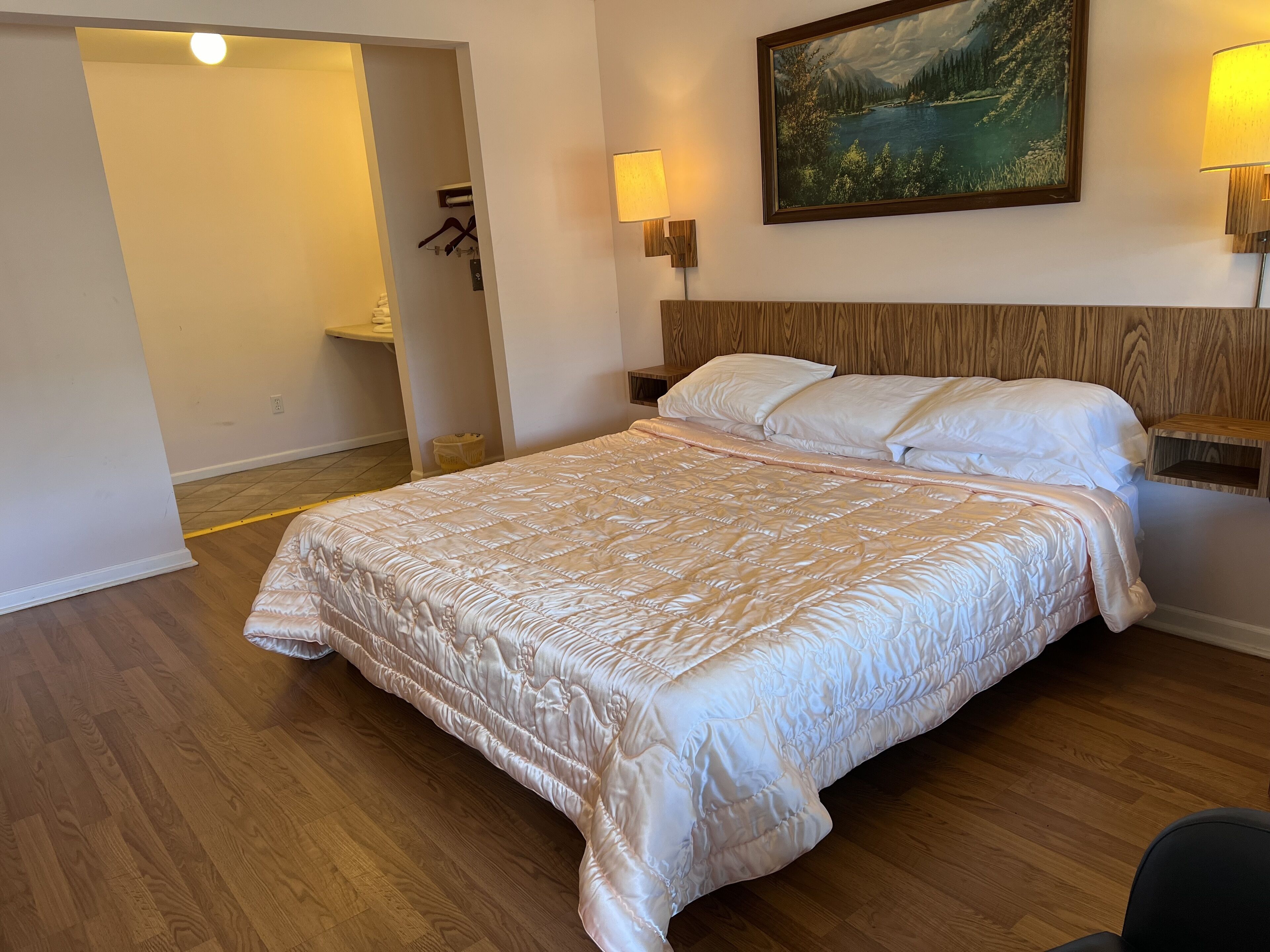 Un dormitorio con una cama grande, cabecera de madera, dos lámparas de noche y un cuadro en la pared.