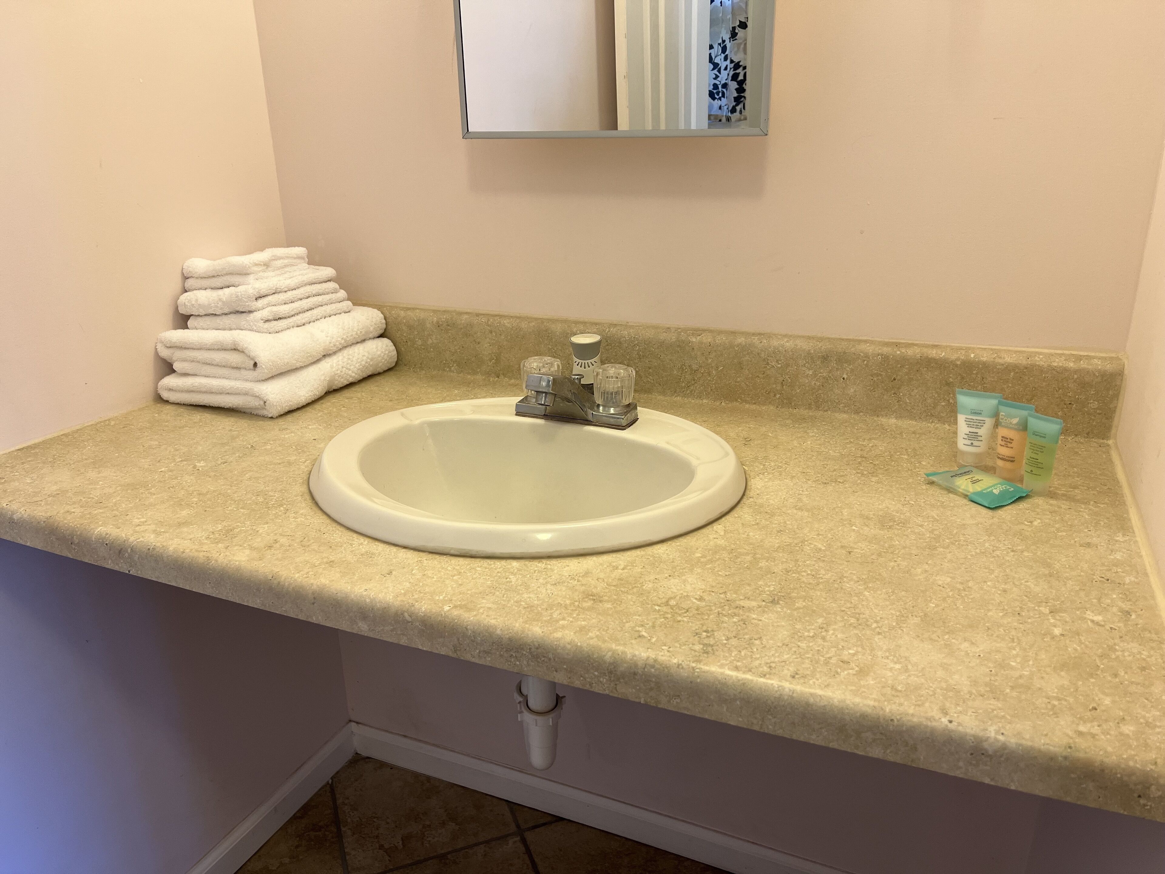A bathroom sink with a beige countertop, a stack of white towels, and toiletries.