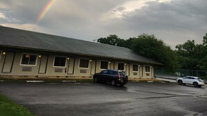 A building with a sloped roof, multiple windows, and a parking lot with two cars. - Glenwood Inn - Stroudsburg (Delaware Water Gap)