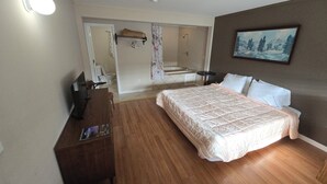 A bedroom with a bed, a desk, a chair, a dresser, and a bathroom visible through an open door. - Glenwood Inn - Stroudsburg (Delaware Water Gap)