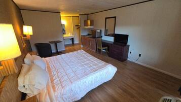 Una habitación de hotel con una cama grande, un escritorio, una silla, un televisor y una pequeña kitchenette.