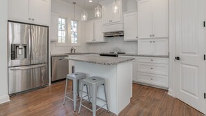 Une cuisine moderne avec des meubles blancs, des appareils en acier inoxydable et un îlot central doté de tabourets.