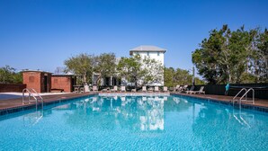 Une piscine à l’eau d’un bleu cristallin, entourée de chaises longues et avec un bâtiment en briques en arrière-plan.