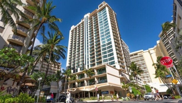 A tall hotel with multiple balconies, palm trees, and a stop sign. - Waikiki Alive & Well, Luxury Suite, Save Over $700 (Honolulu)