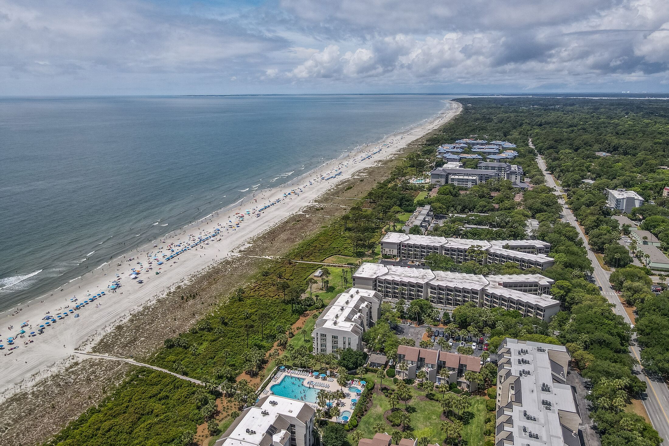 An aerial view of a coastal hotel with a beach, multiple buildings, and a swimming pool.