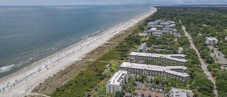 Vue aérienne d’un hôtel situé sur la côte, avec une plage, plusieurs bâtiments et une piscine.