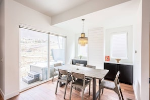 A dining area with a wooden table and chairs, a chandelier, and a view through a sliding glass door.
