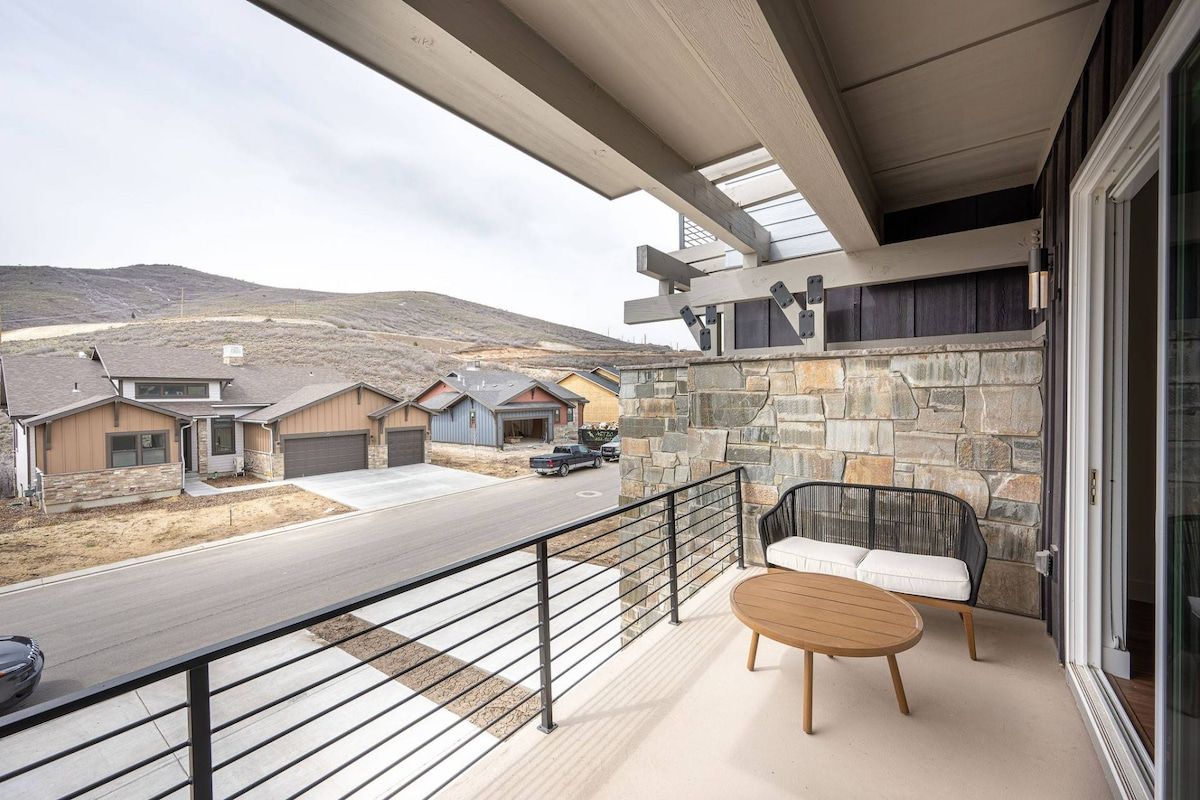 A balcony with a stone wall, a wooden table, and a black metal railing.