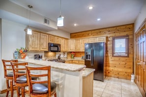 Una cocina con armarios de madera, un refrigerador de acero inoxidable, un microondas y una encimera de granito.
