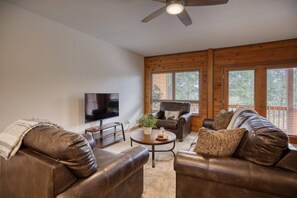 A living room with leather sofas, a coffee table, a television, and a ceiling fan.