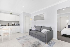 Eine moderne Wohnung mit Küchenzeile, einem grauen Sofa, einem kleinen Esstisch und einem Bett.