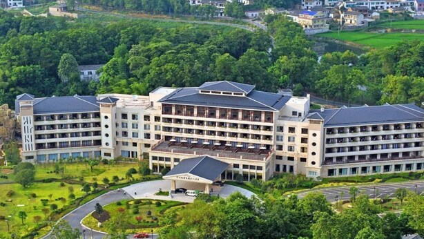 A multi-story hotel with a central courtyard, surrounded by lush greenery and residential buildings. - Huitang Zilongwan Hot Spring Holiday Hotel (Changsha)