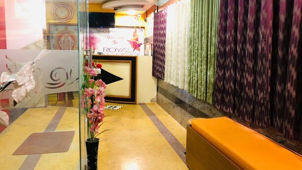 A reception area with a glass partition, a reception desk, a wall-mounted television, and a patterned curtain. - Royal Residency (Sriperumbudur)