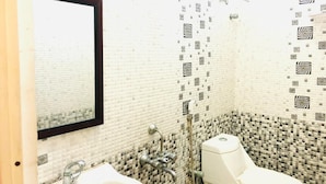 A bathroom with a white sink, a mirror, and a toilet. The walls are covered with patterned tiles. - Royal Residency (Sriperumbudur)