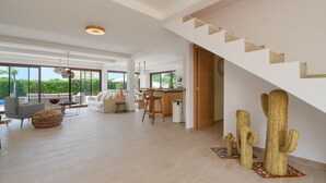 A spacious living area with a modern kitchen, a staircase, and a view of greenery.