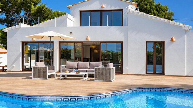 A modern two-story house with a swimming pool, outdoor furniture, and large windows.