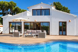 Une maison moderne à deux étages, dotée d’une piscine, de mobilier d’extérieur et de grandes fenêtres.