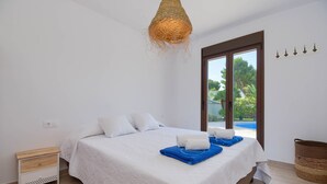 A bedroom with a bed, a nightstand, a wicker basket, and a view of an outdoor swimming pool.