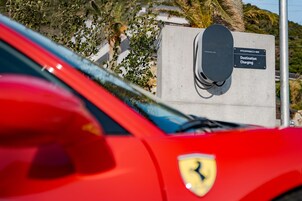 Un auto rojo estacionado cerca de una estación de carga, con un cartel que indica que es para carga de destino Porsche.