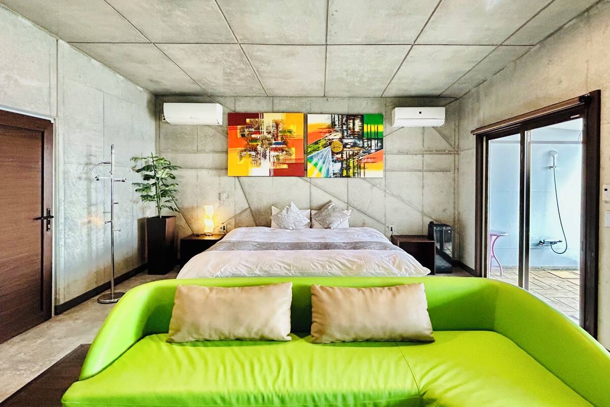 A modern bedroom with a bed, green sofa, and a large window.