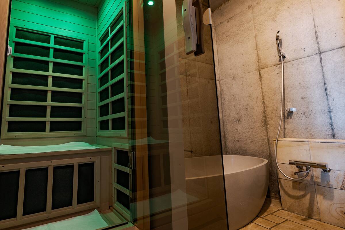 A sauna room with a bench, a glass door, and a shower area with a bathtub.