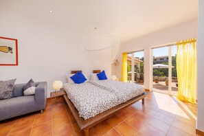 Un dormitorio con cama, sofá, mesita de noche y un amplio ventanal con cortinas.