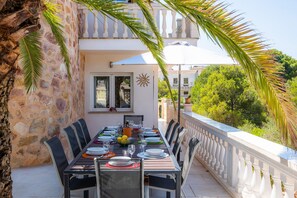 Una mesa de comedor al aire libre con sillas, una sombrilla blanca y una pared de piedra.