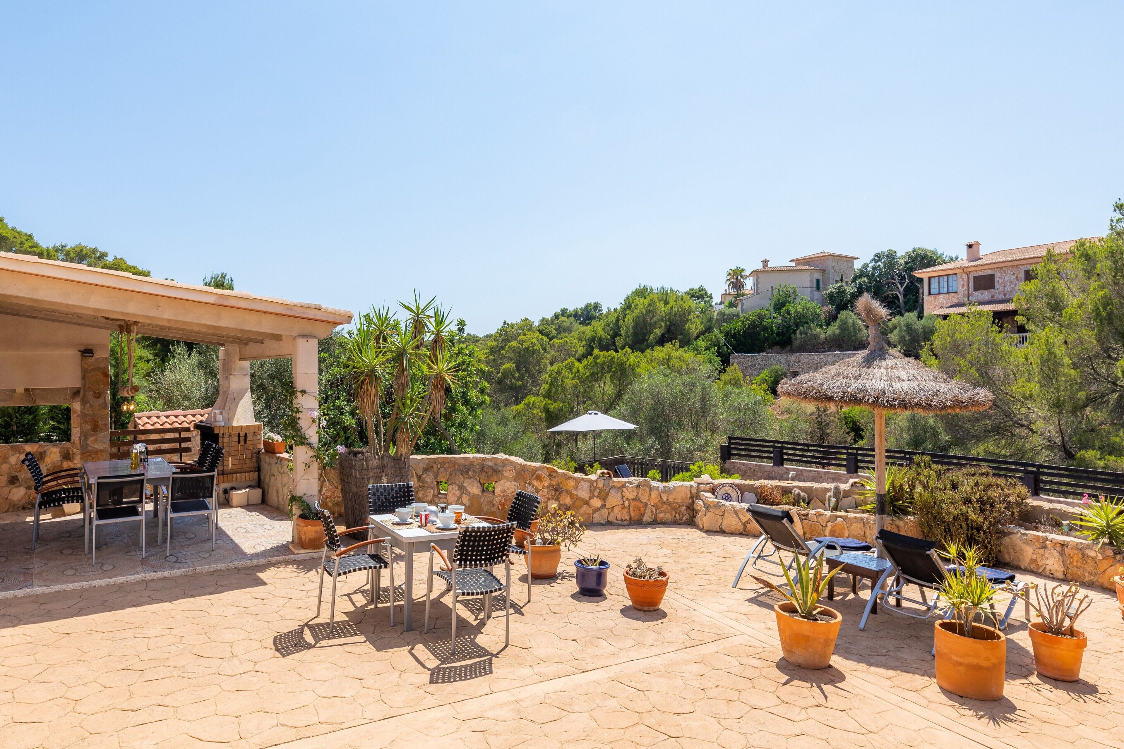 An outdoor patio with stone flooring, metal chairs, a table, potted plants, and a thatched umbrella.