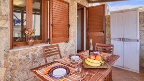 A stone building with wooden shutters, a table set with plates, a bottle, and fruit. - Apartment " Marina Freedom" with Wi-Fi, Air Conditioning, Balcony & Terrace (Cagliari)