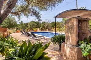 A swimming pool with lounge chairs, surrounded by greenery and a stone structure.