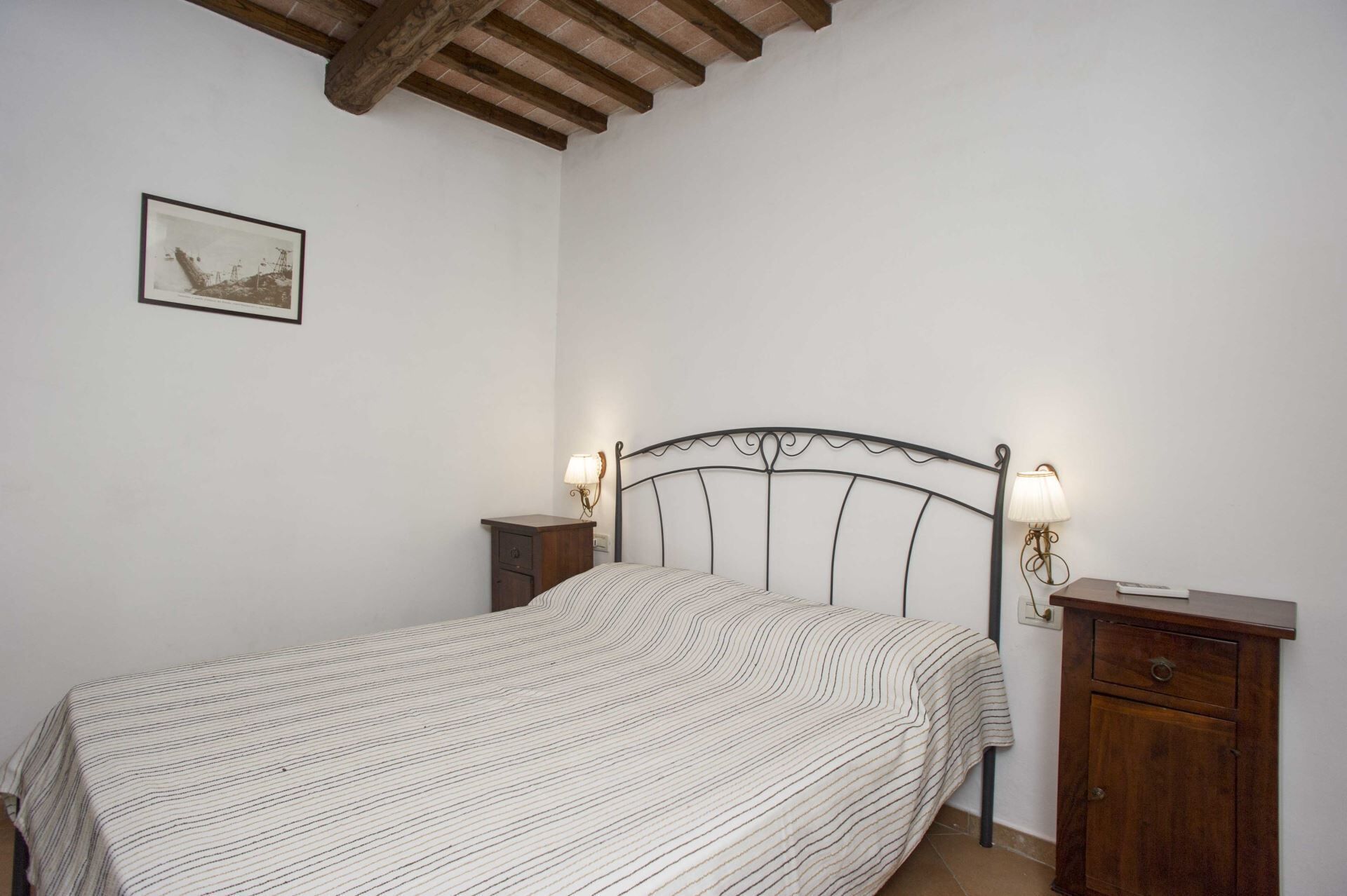 A bedroom with a bed, two bedside tables, a nightstand, a lamp, and a framed picture on the wall.