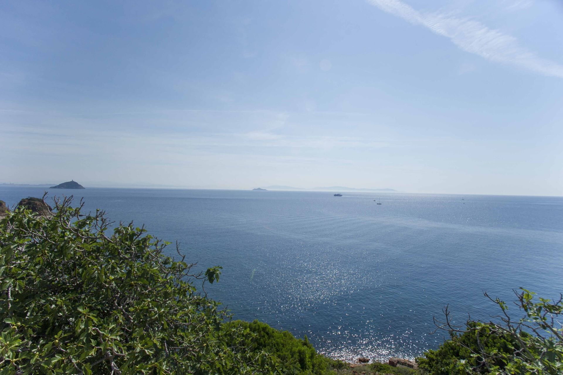 A coastal landscape with a clear view of the sea, distant islands, and a ship.