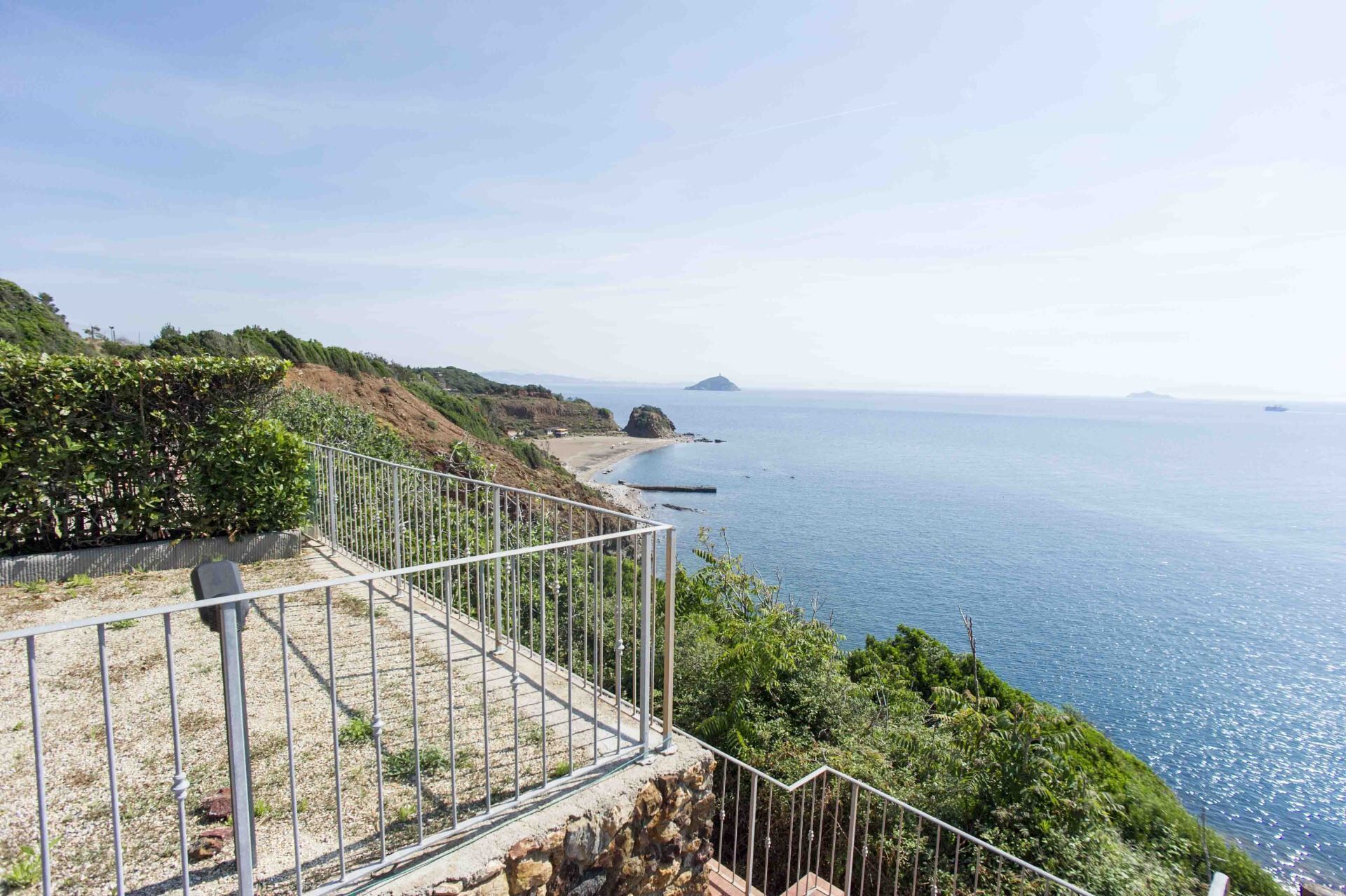 A coastal view with a metal railing overlooking the sea, a rocky cliff, and a distant island.