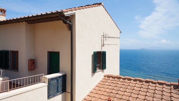 A coastal building with a tiled roof, a green door, and a view of the sea. - RESIDENZA LA SCOGLIERA - MONO N° 6 LA SCOGLIERA (Rio Marina)
